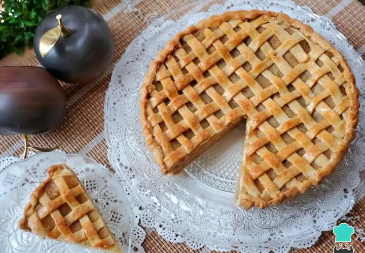 Tarta de manzana de la abuela, dorada y con un enrejado perfecto. Un trozo ya servido en un plato de cristal.