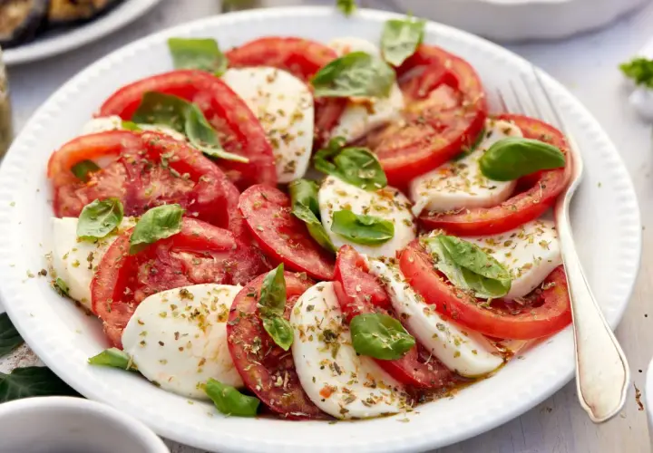 Ensalada caprese fresca con rodajas de tomate y mozzarella, aderezada con albahaca y especias.