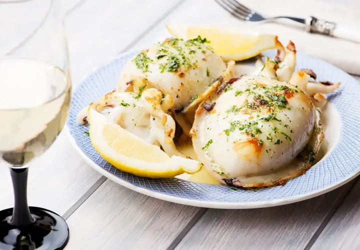 Delicioso sepia a la plancha, servido con gajos de limón y perejil picado, acompañado de una copa de vino blanco.