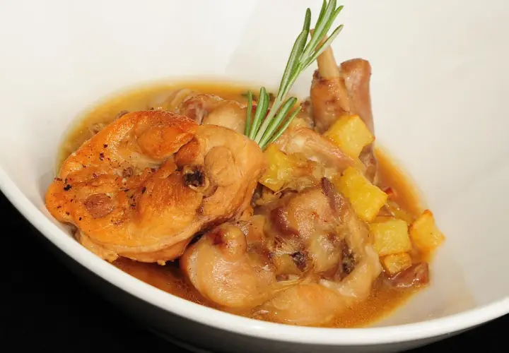 Delicioso conejo en salsa con patatas y romero, servido en un cuenco blanco.