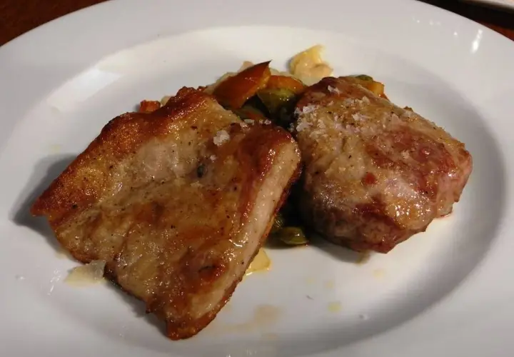 Dos trozos de secreto de cerdo a la plancha, dorados y jugosos, servidos con verduras salteadas en un plato blanco.