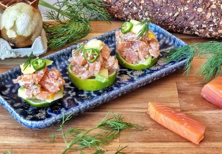 Tartar de salmón fresco servido en mitades de lima, adornado con aguacate y jalapeño.