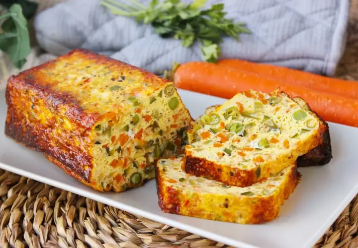 Pastel de verduras al horno, con trozos de zanahoria y guisantes, servido en una bandeja blanca.