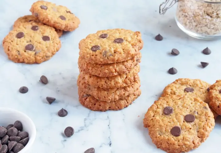Deliciosas galletas de avena y chocolate, apiladas y esparcidas, con chispas de chocolate y avena en un frasco.