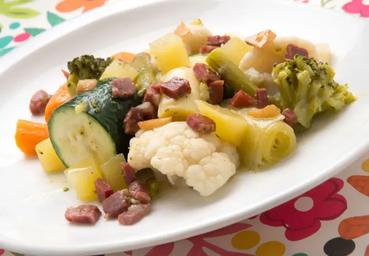 Un colorido panache de verduras con brócoli, coliflor, calabacín, zanahoria y patatas, salpicado de trocitos de jamón.