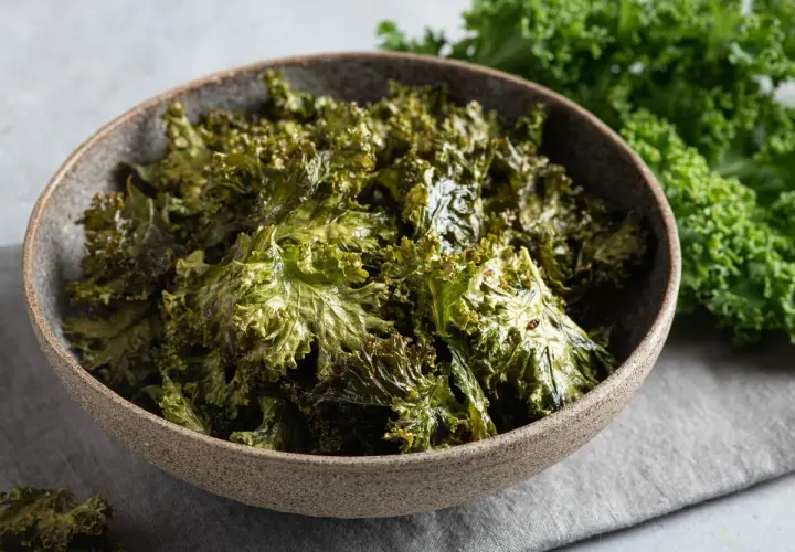Crujientes chips de kale horneados en un tazón, perfectos para tus recetas con kale.