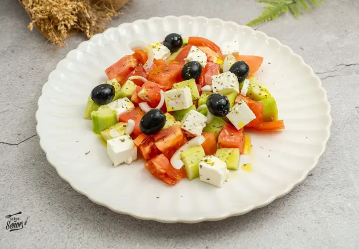 Ensalada griega fresca con tomates, pepinos, cebolla, aceitunas negras y queso feta en cubos, aderezada con aceite de oliva y hierbas.