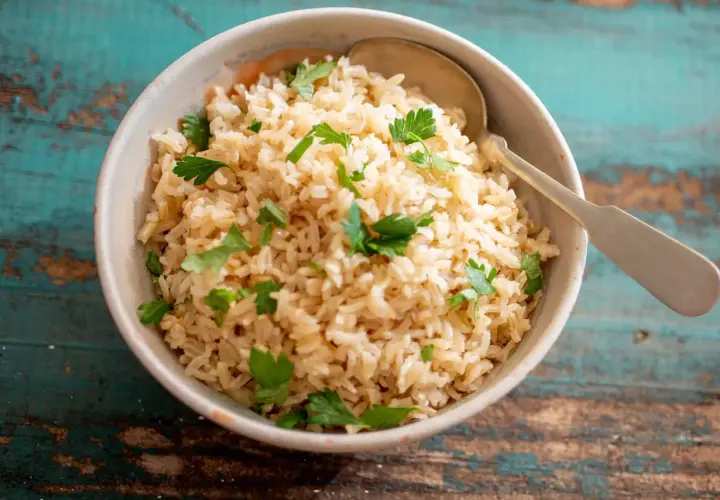 Un tazón de arroz integral esponjoso, perfecto para aprender como hacer arroz integral. Decorado con perejil fresco y una cuchara lista para servir.