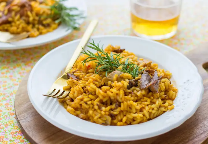 Delicioso arroz con secreto ibérico y setas, adornado con romero fresco. Un plato reconfortante y lleno de sabor.