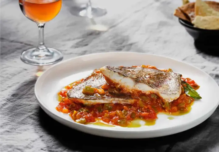 Delicioso plato de urta a la roteña, con pescado blanco y verduras en salsa, acompañado de una copa de vino.