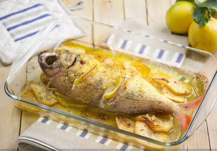 Besugo al horno con patatas y limón, recién sacado del horno en una fuente de cristal.