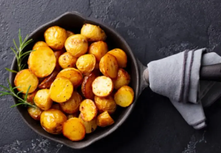 Patatas doradas y tiernas listas para cocer, con romero fresco en una sartén de hierro fundido.