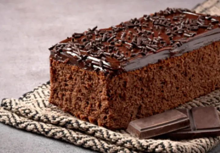 Un delicioso pastel de chocolate cubierto con glaseado y chispas de chocolate, acompañado de trozos de chocolate.