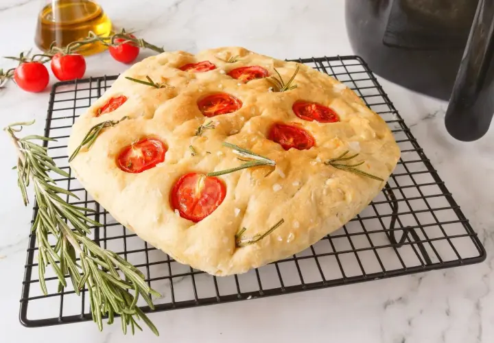 Focaccia receta casera con tomates cherry y romero sobre una rejilla.