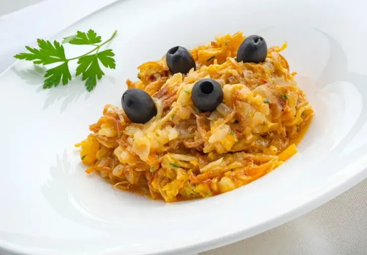 Delicioso revuelto de bacalao con aceitunas negras y perejil fresco, servido en un plato blanco.