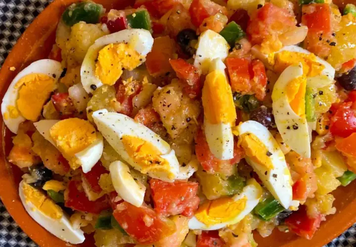 Ensalada campera con patatas, huevos duros, tomate, pimiento y aceitunas negras, todo mezclado y sazonado.