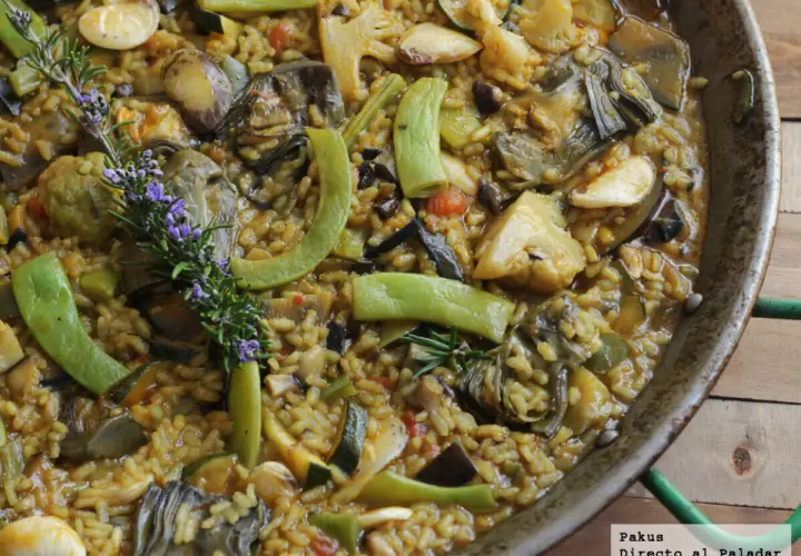 Paella de verduras vibrante, con alcachofas, calabacín, pimientos y romero fresco. Un festín para la vista y el paladar.
