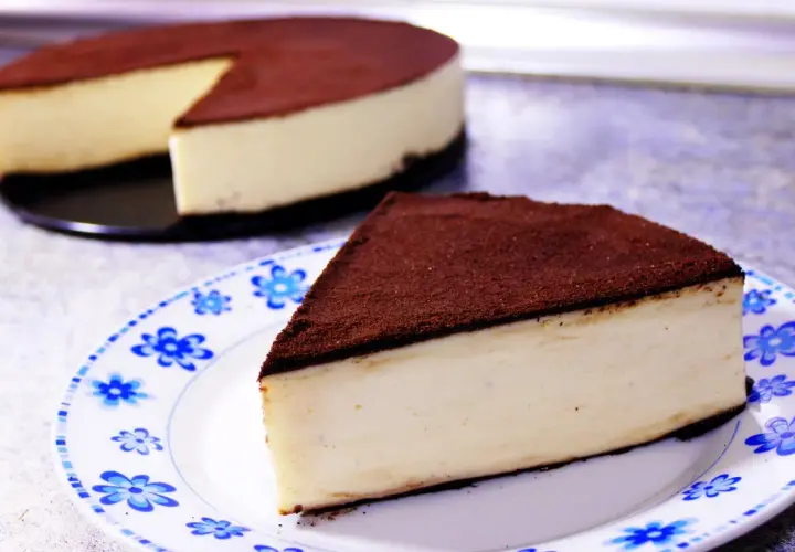 Un delicioso pastel de queso cubierto de cacao, perfecto para postres fáciles. Una rebanada servida en un plato con flores azules.