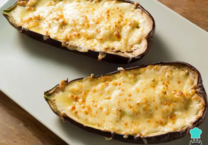 Dos mitades de berenjenas rellenas de carne, gratinadas con queso dorado y burbujeante, listas para disfrutar.