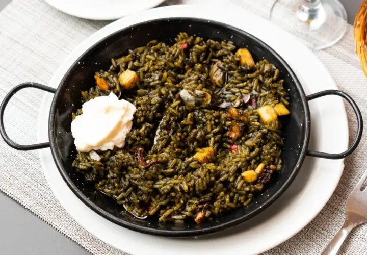 Arroz negro con sepia, servido en paellera con una cucharada de alioli. Se aprecian trozos de sepia y pimientos.
