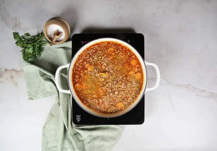 Olla con lentejas con arroz y zanahoria hirviendo. Al lado, perejil fresco y un cuenco de sal.