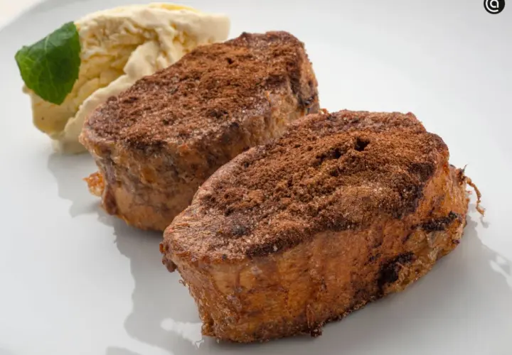 Dos torrijas de chocolate espolvoreadas con cacao y azúcar, acompañadas de helado de vainilla y una hoja de menta.