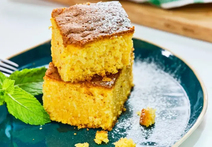 Dos porciones de bizcocho de calabaza apiladas, espolvoreadas con azúcar glas, junto a hojas de menta fresca en un plato azul.