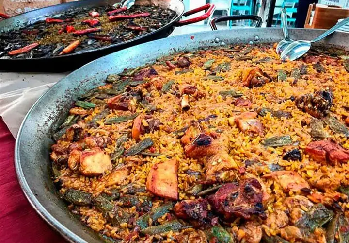 Paella valenciana con pollo, conejo y verduras. Los ingredientes se mezclan con el arroz en esta gran paellera.