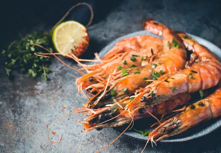 Gambones al horno, jugosos y dorados, servidos con hierbas frescas y rodaja de limón.