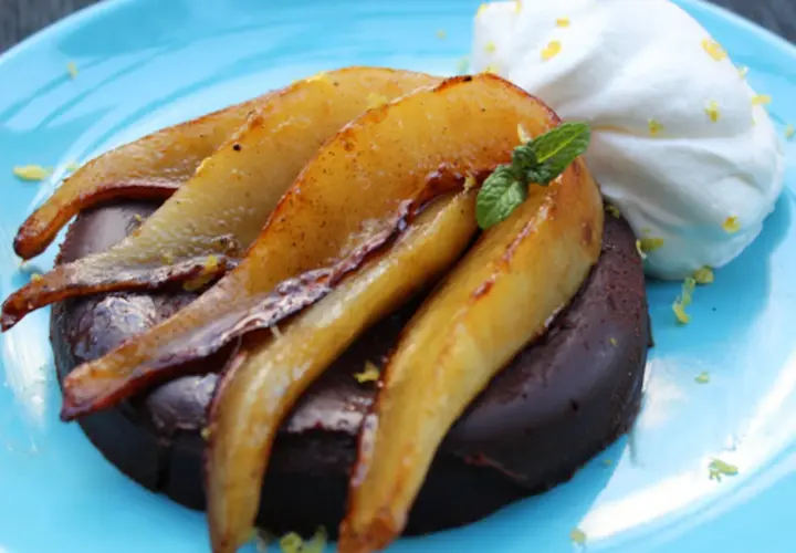 Deliciosa marquesa de chocolate con peras caramelizadas y crema batida, adornada con menta y ralladura de limón.