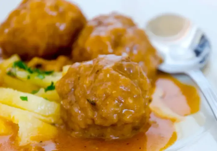 Albondigas a la jardinera, jugosas y cubiertas de salsa, acompañadas de patatas y perejil. Un plato casero listo para disfrutar.