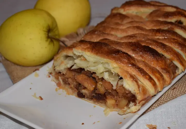 Un delicioso strudel de manzana recién horneado, con su masa dorada y crujiente, relleno de trozos de manzana y pasas.