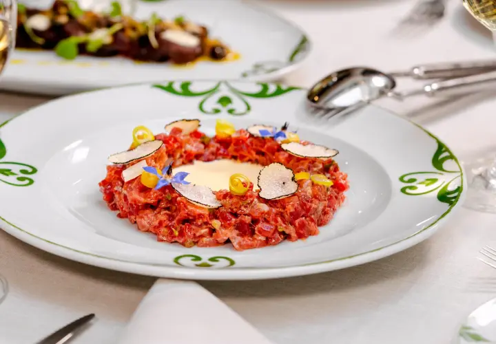 Delicioso tartar de atún fresco, adornado con láminas de trufa negra, flores comestibles y un toque de limón.