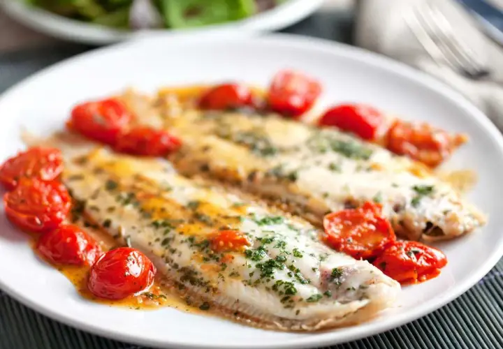 Dos filetes de lenguado a la plancha, servidos con tomates cherry salteados y perejil picado.
