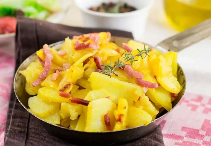 Patatas al microondas con trocitos de bacon crujiente y romero fresco, servidas en una sartén metálica.