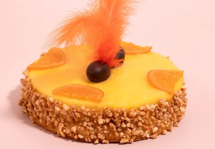 Deliciosa mona de Pascua catalana con glaseado amarillo, rodajas de naranja, chocolate y plumas naranjas.
