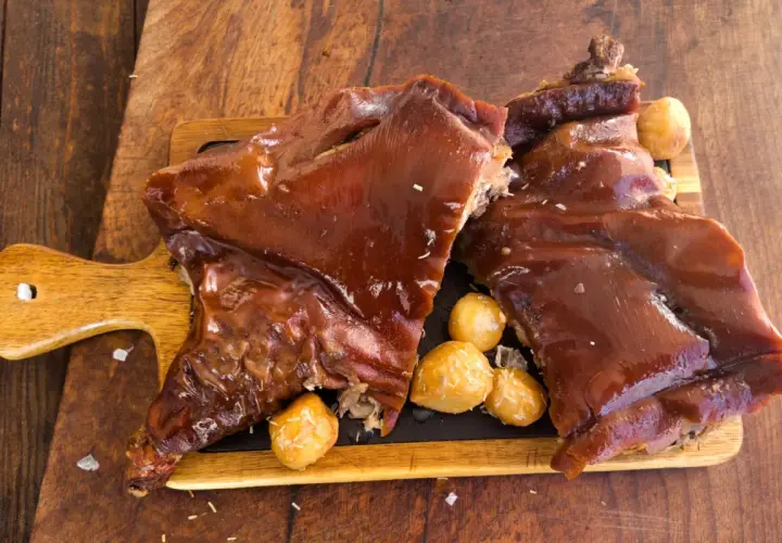 Delicioso cochinillo al horno, receta de la abuela, servido con patatas asadas sobre tabla de madera.