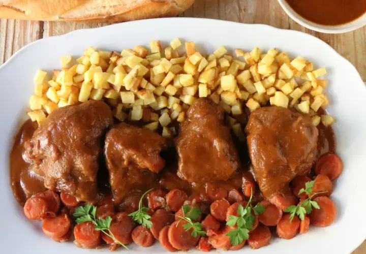 Delicioso jarrete de ternera estofado, acompañado de patatas fritas crujientes y zanahorias en rodajas.