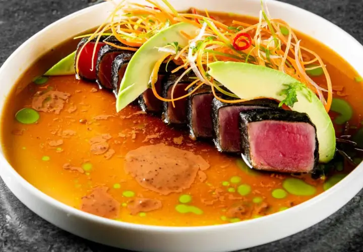 Tataki de atún sellado, servido en un caldo vibrante con aguacate, zanahoria rallada y un toque picante.