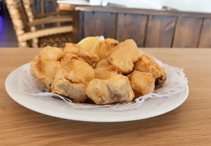 Plato de cazon en adobo, trozos de pescado frito y dorado, servido con una rodaja de limón.