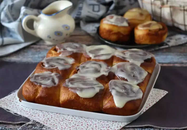 Deliciosos rollitos de canela recién horneados, cubiertos con un glaseado blanco cremoso, listos para ser disfrutados.
