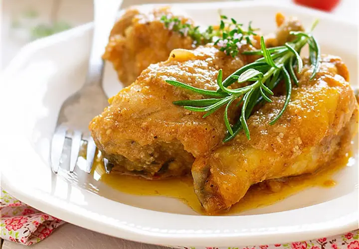 Pollo en salsa de la abuela, jugoso y dorado, servido en plato blanco con romero fresco. Un clásico casero.