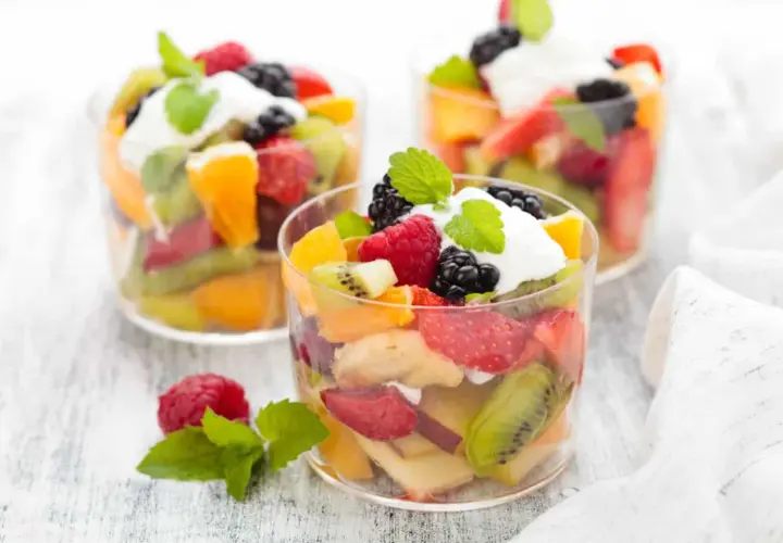 Deliciosa macedonia de frutas con fresas, kiwi, naranja, frambuesas y moras, coronada con crema y menta.