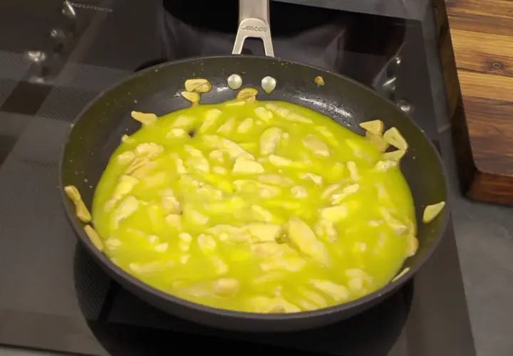 El bacalao al pil pil burbujea en la sartén, con trozos de ajo dorándose en el aceite.
