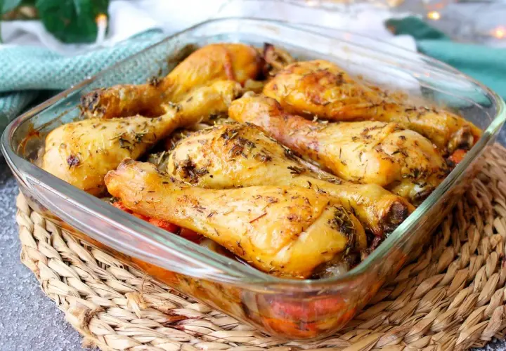 Muslos de pollo al horno dorados y jugosos, sazonados con hierbas aromáticas, servidos en una fuente de vidrio.