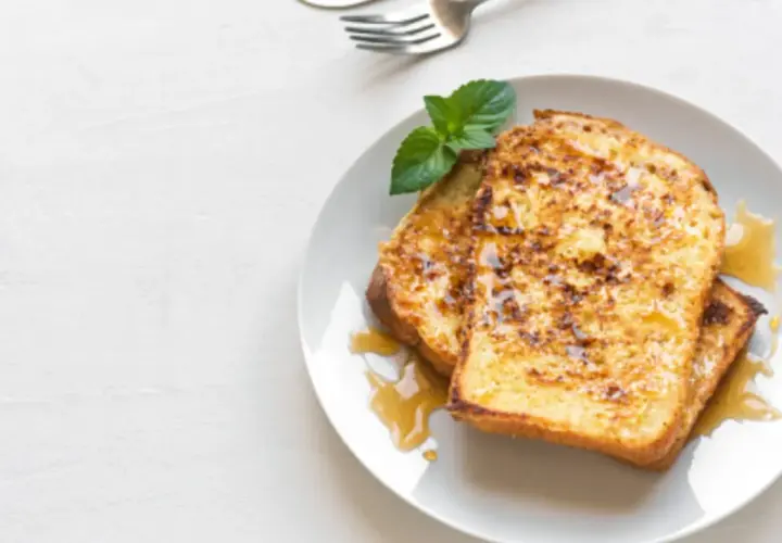Dos rebanadas de tostada francesa dorada, bañadas en sirope y decoradas con menta. Una deliciosa french toast receta para el desayuno.