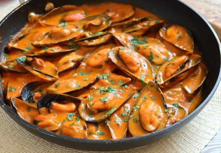 Mejillones con tomate en salsa cremosa, espolvoreados con perejil fresco. Un plato delicioso y fácil de preparar.