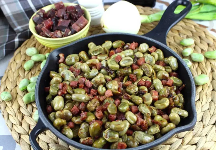 Habas tiernas salteadas con trocitos de jamón en una sartén de hierro fundido, un plato tradicional lleno de sabor.