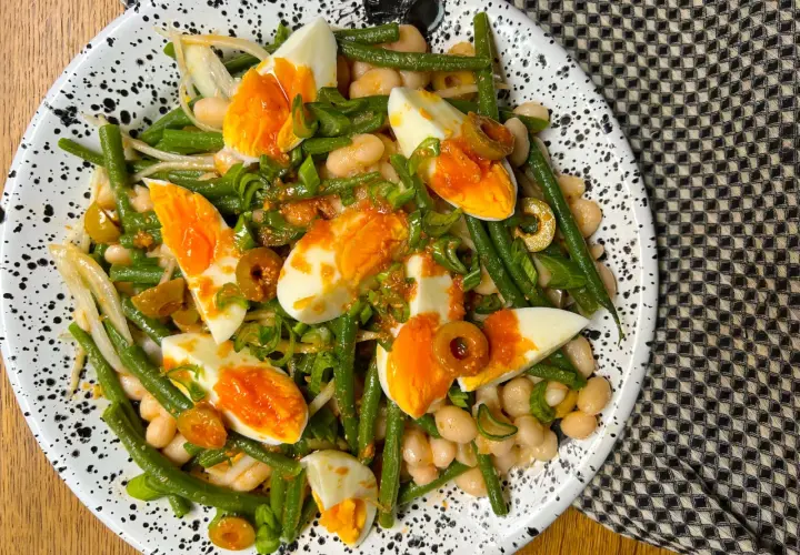 Ensalada de judías verdes, huevos duros, alubias blancas y aceitunas, aderezada con cebolleta picada.