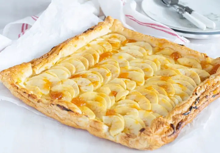 Tarta de manzana con crema pastelera, con finas láminas de manzana y un glaseado dorado sobre hojaldre crujiente.